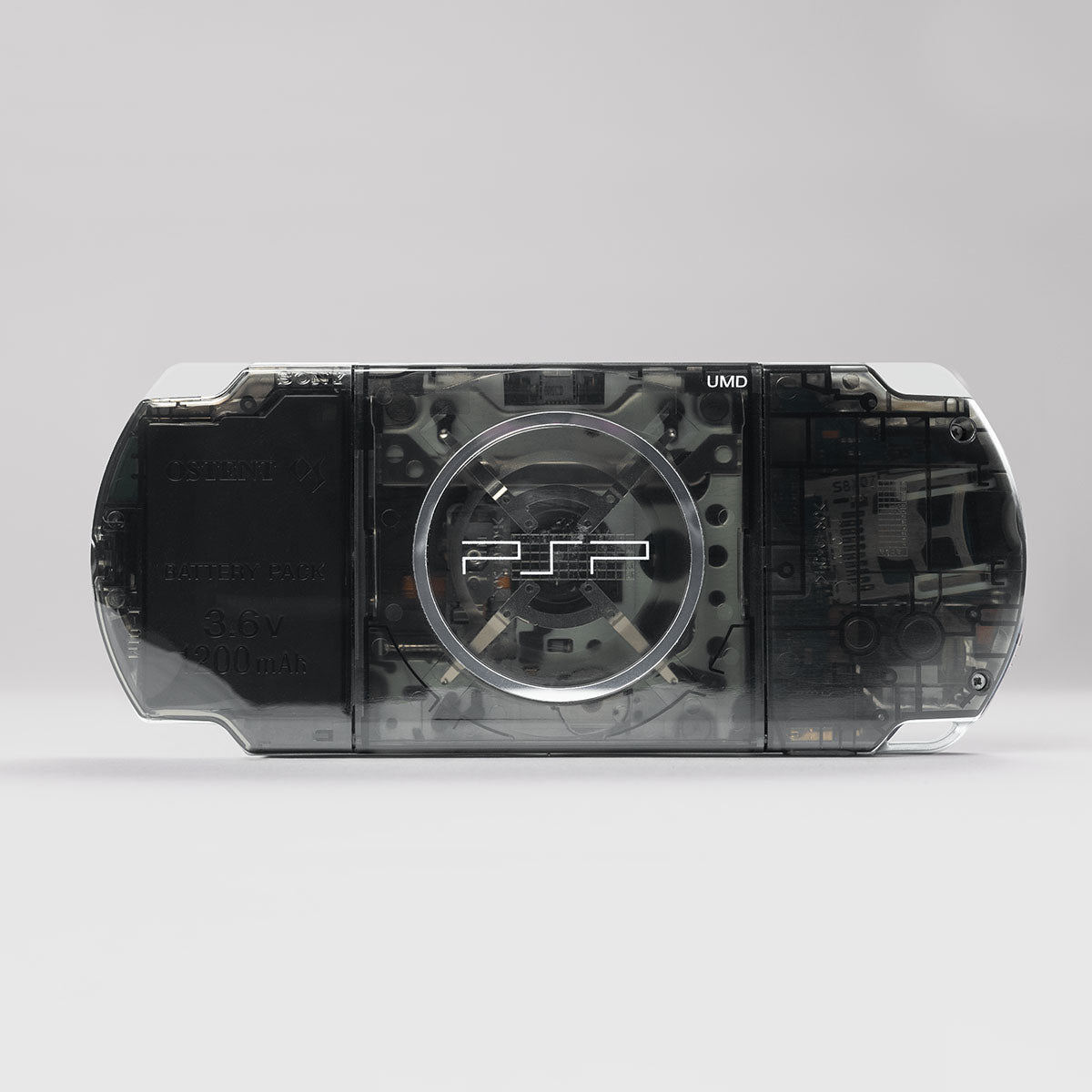 Back view of a black transparent Sony PSP featuring a visible UMD drive and an OSTENT 3.6V 2200mAh battery pack inside a custom clear shell