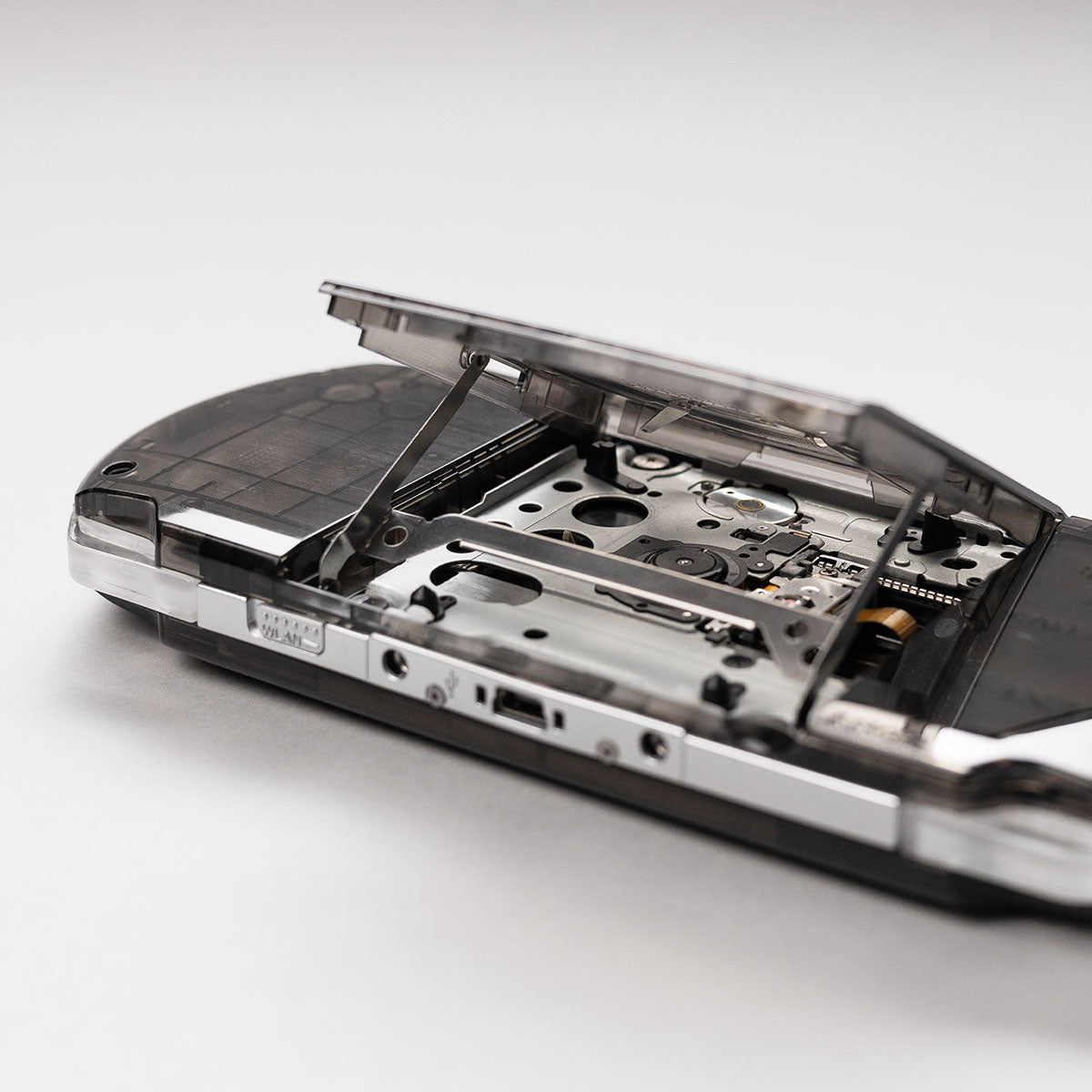 Detailed view of a black transparent Sony PSP with the UMD drive open, showing the laser mechanism and disc tray assembly