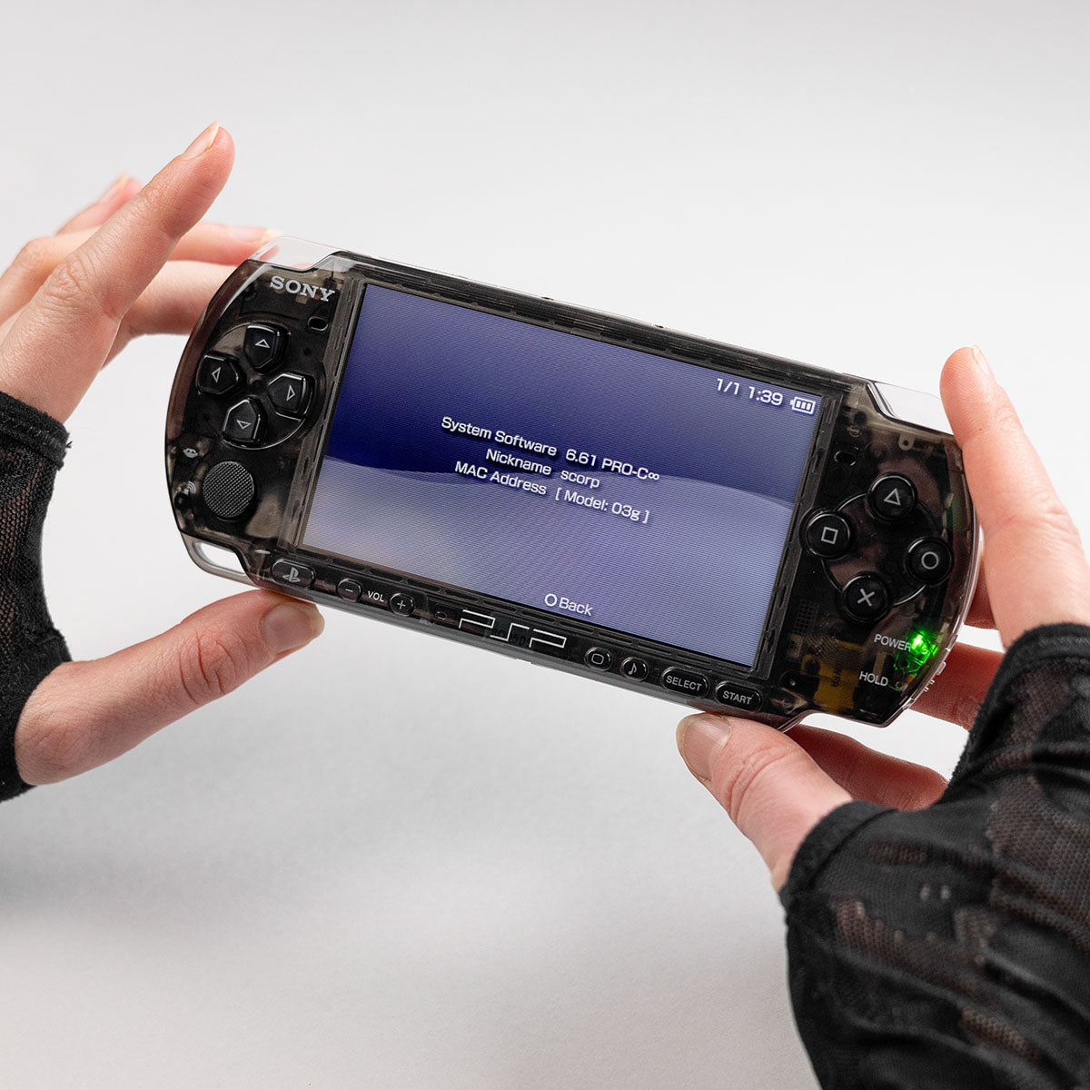 Black transparent Sony PSP running system software 6.61 PRO-C, held in gloved hands with screen showing system info and green power indicator