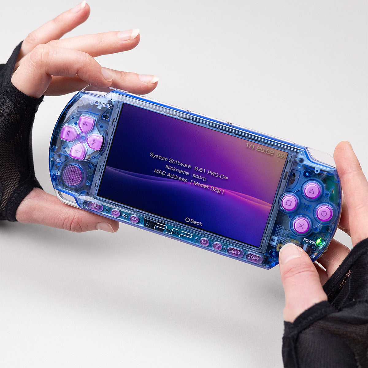 Blue transparent PSP console with pink buttons running firmware 6.61 PRO-C, held in hands and displaying system info on a purple-themed screen
