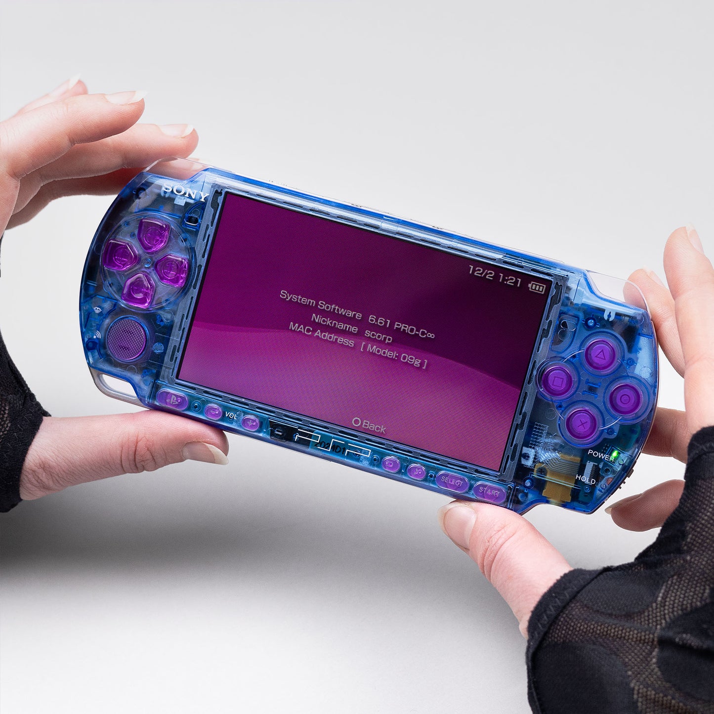 Blue transparent PSP console with pink buttons running firmware 6.61 PRO-C, held in hands and displaying system info on a purple-themed screen