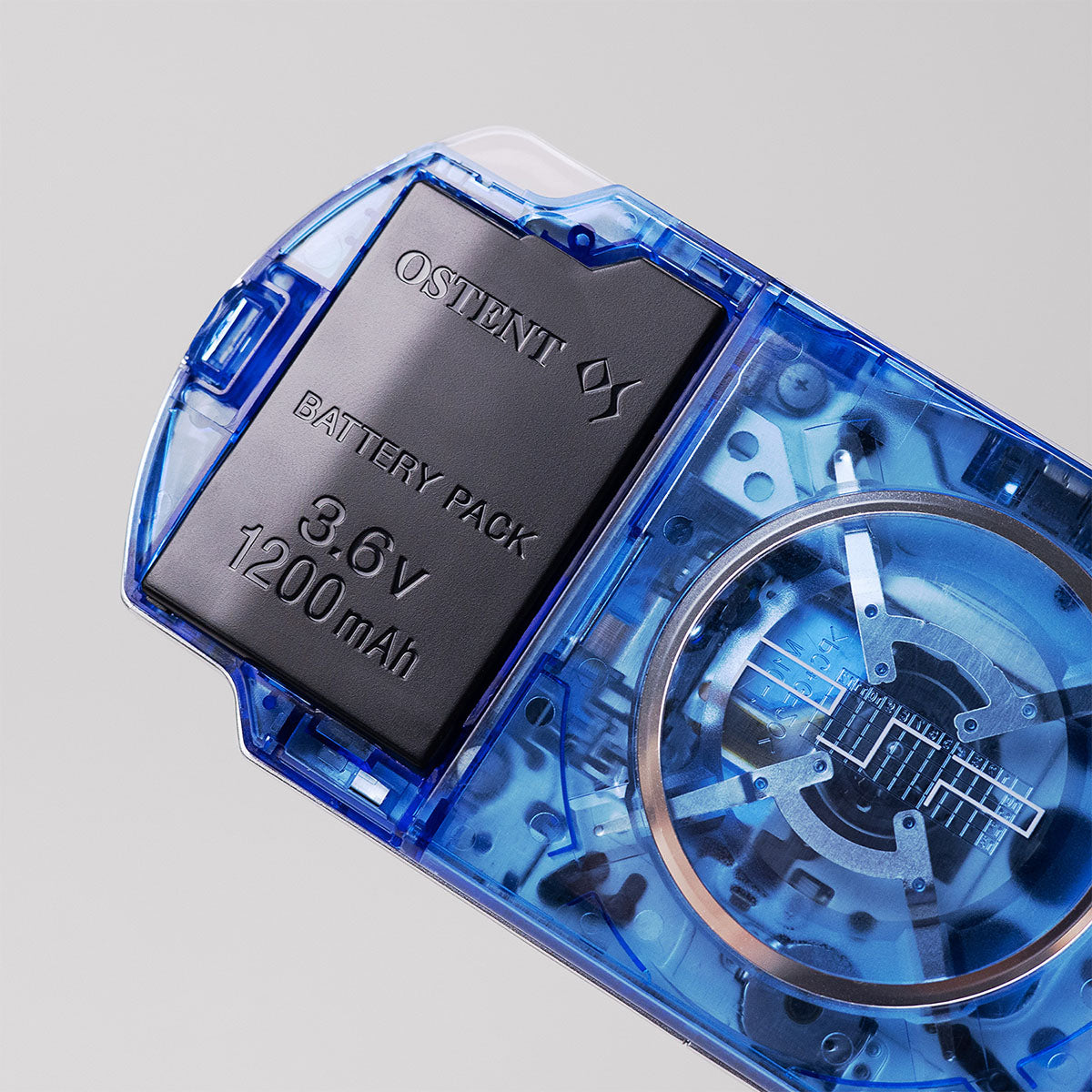 Close-up of a blue transparent PSP showing OSTENT 3.6V 1200mAh battery pack and UMD drive internals beneath the custom clear shell