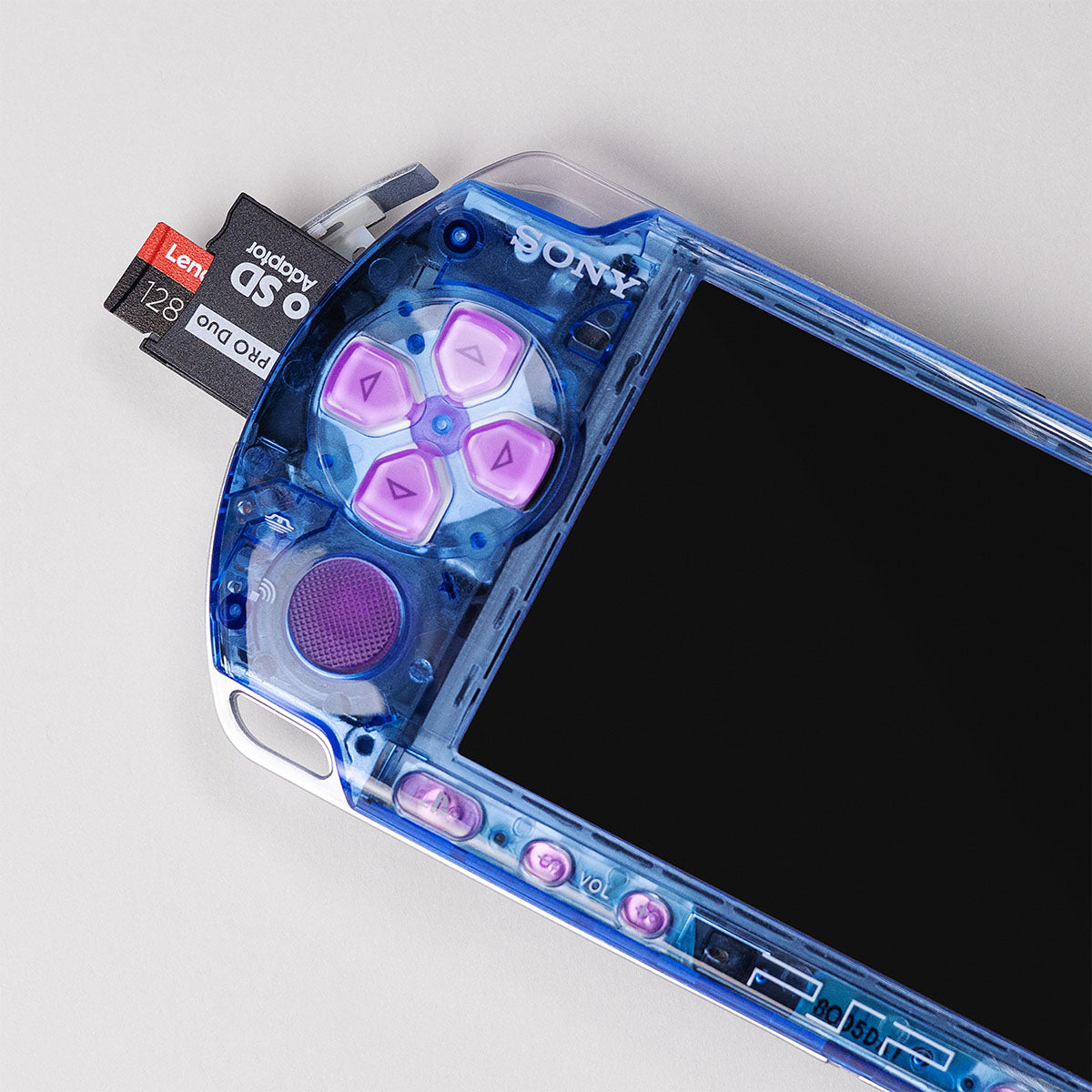Close-up of a blue transparent PSP with pink buttons and a 128GB Lexar microSD card inserted into a Memory Stick Pro Duo adapter