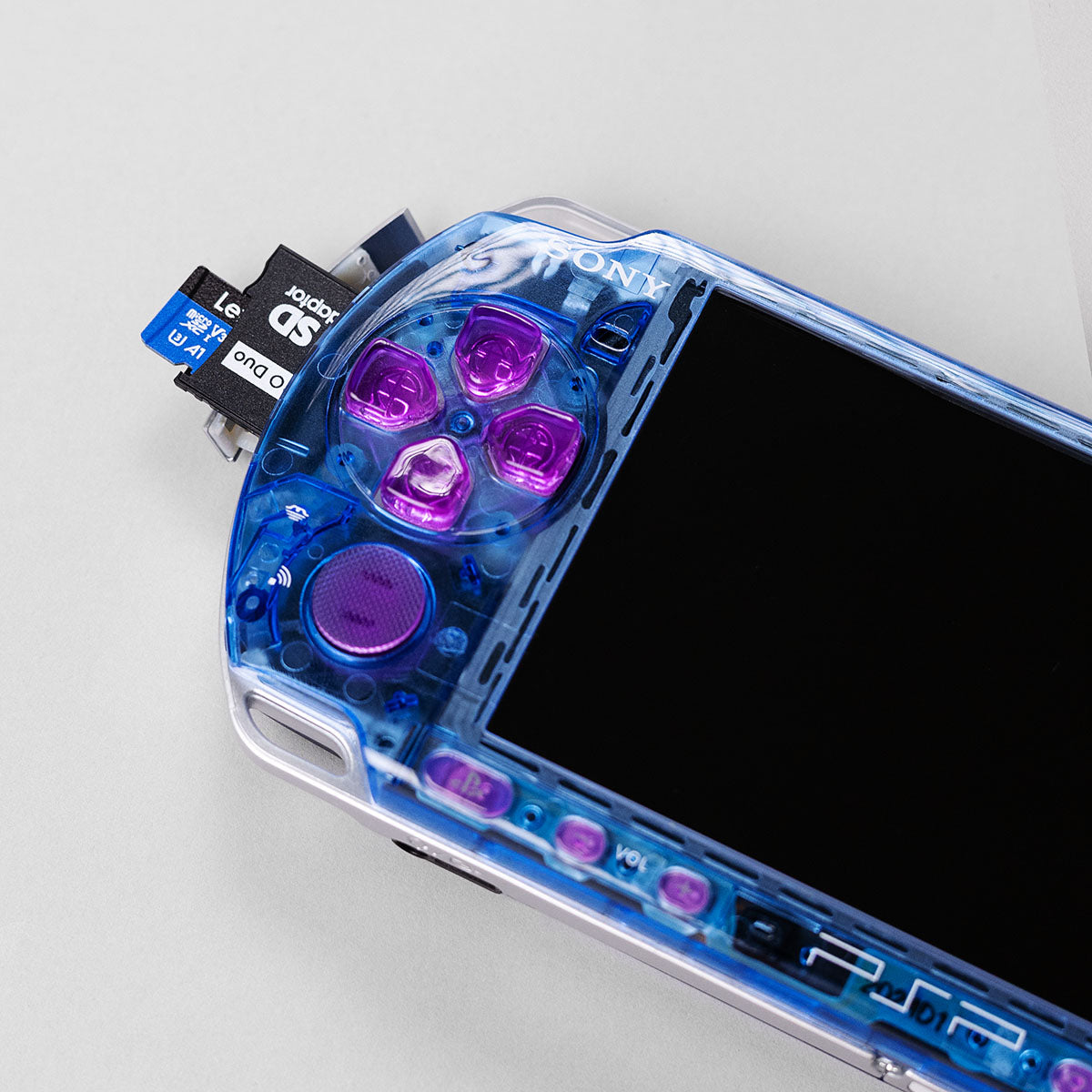 Close-up of a blue transparent PSP with pink buttons and a 128GB Lexar microSD card inserted into a Memory Stick Pro Duo adapter