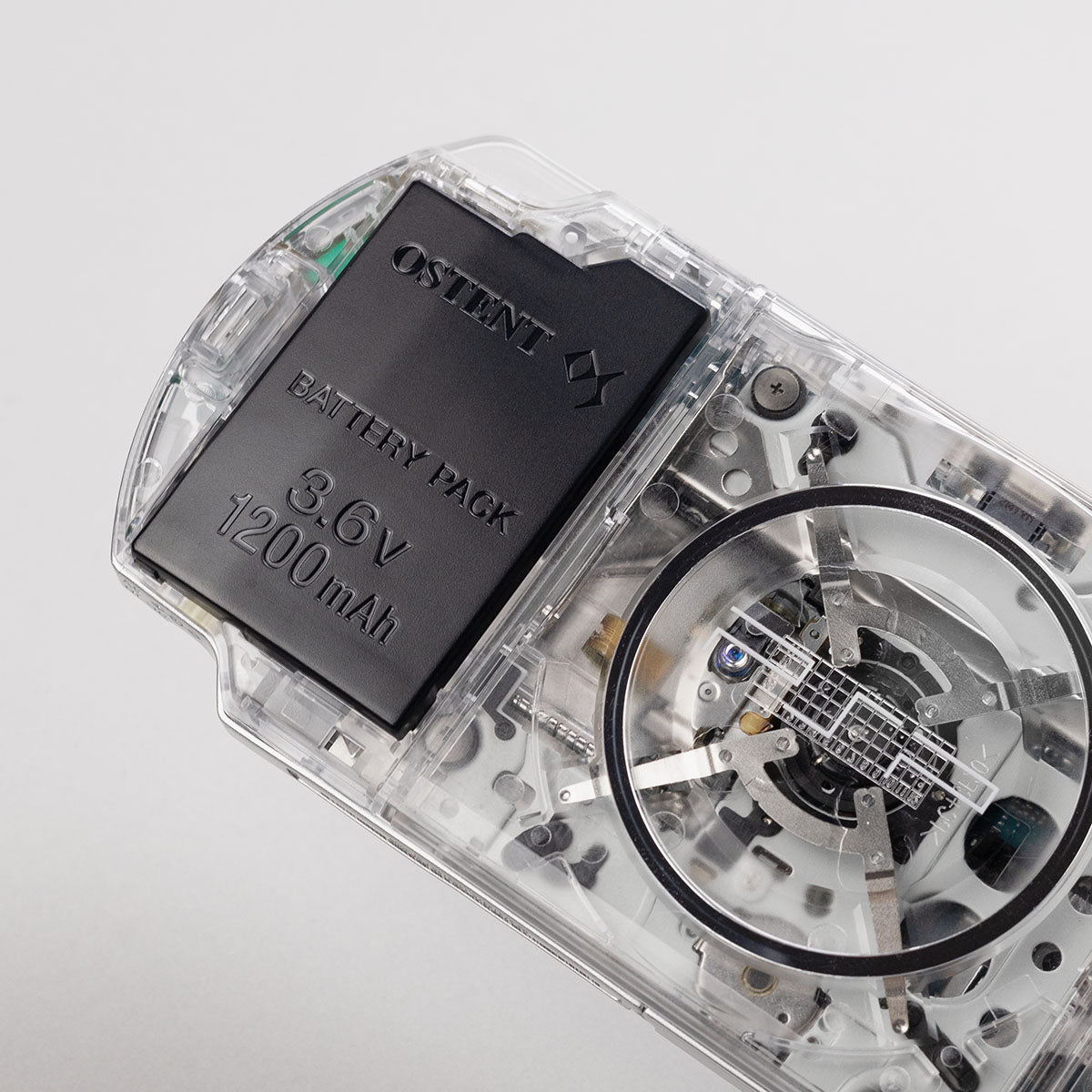 Close-up of a clear transparent Sony PSP showing OSTENT 3.6V 1200mAh battery and UMD drive internals through the shell
