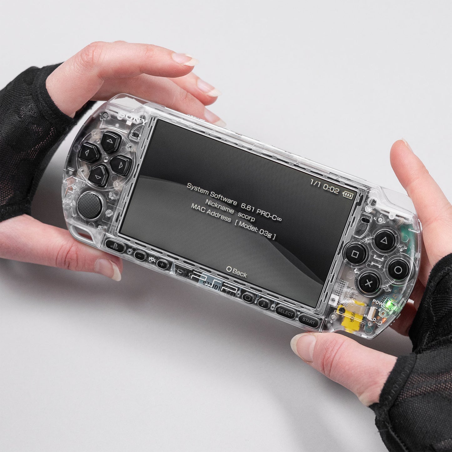 Sony PSP handheld console running firmware 6.61 PRO-C with a custom transparent clear shell, held in hands wearing black gloves