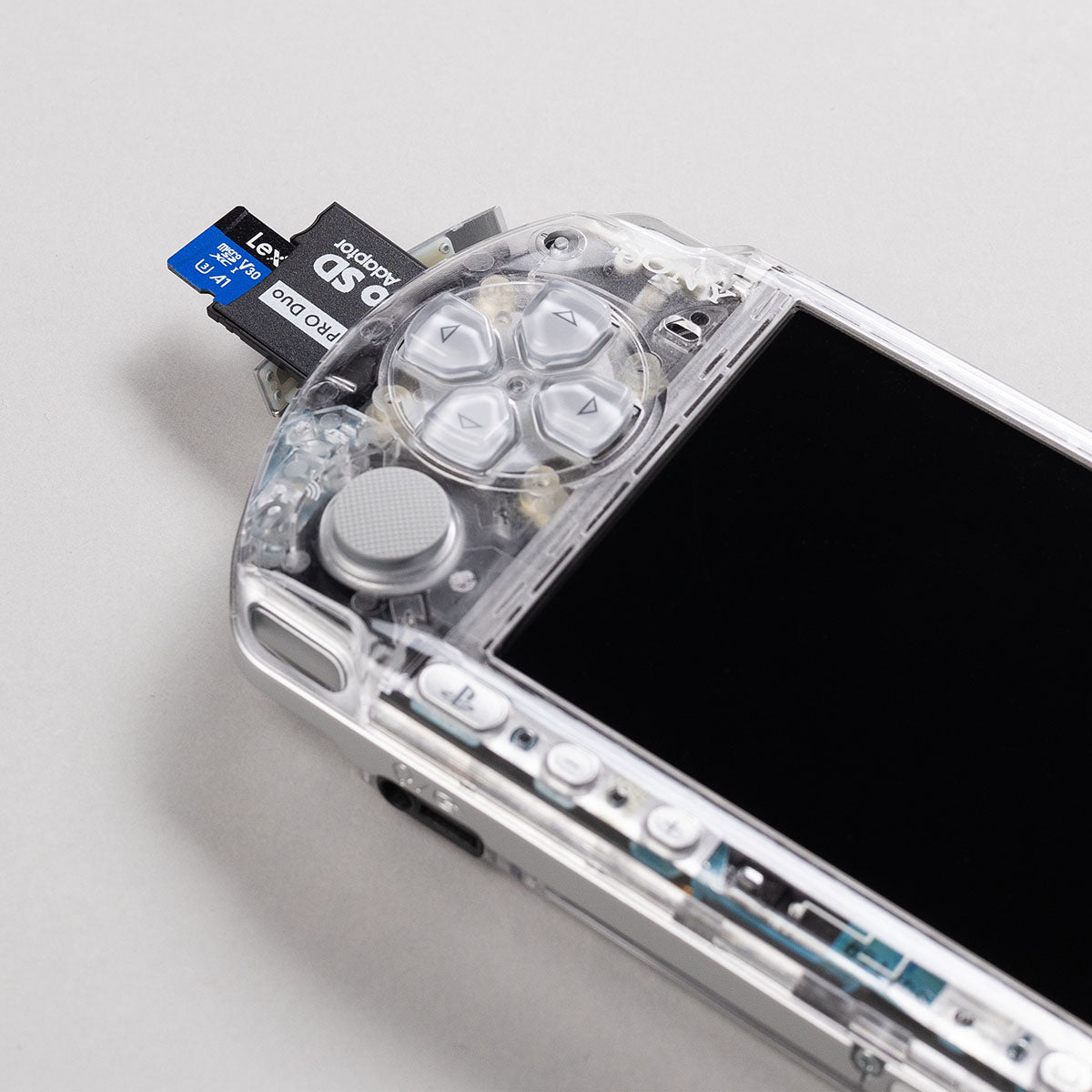 Close-up of a clear Sony PSP with grey buttons and a dual microSD to Memory Stick Pro Duo adapter inserted for expanded storage