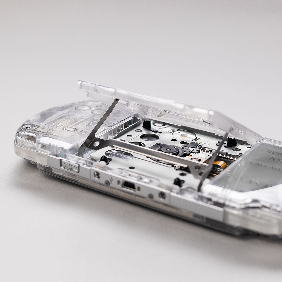 Close-up of a transparent clear shell Sony PSP with the UMD drive open, showing internal laser assembly and disc tray mechanism in detail