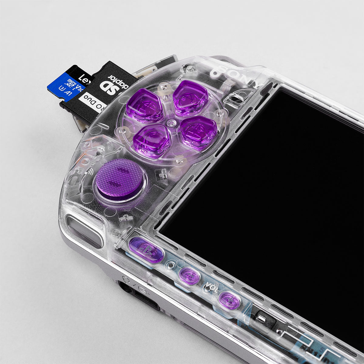 Close-up of clear PSP-3000 with purple D-pad and Lexar SD adapter inserted. Custom mod showing precision detail and dual memory setup by PlayingScorp.
