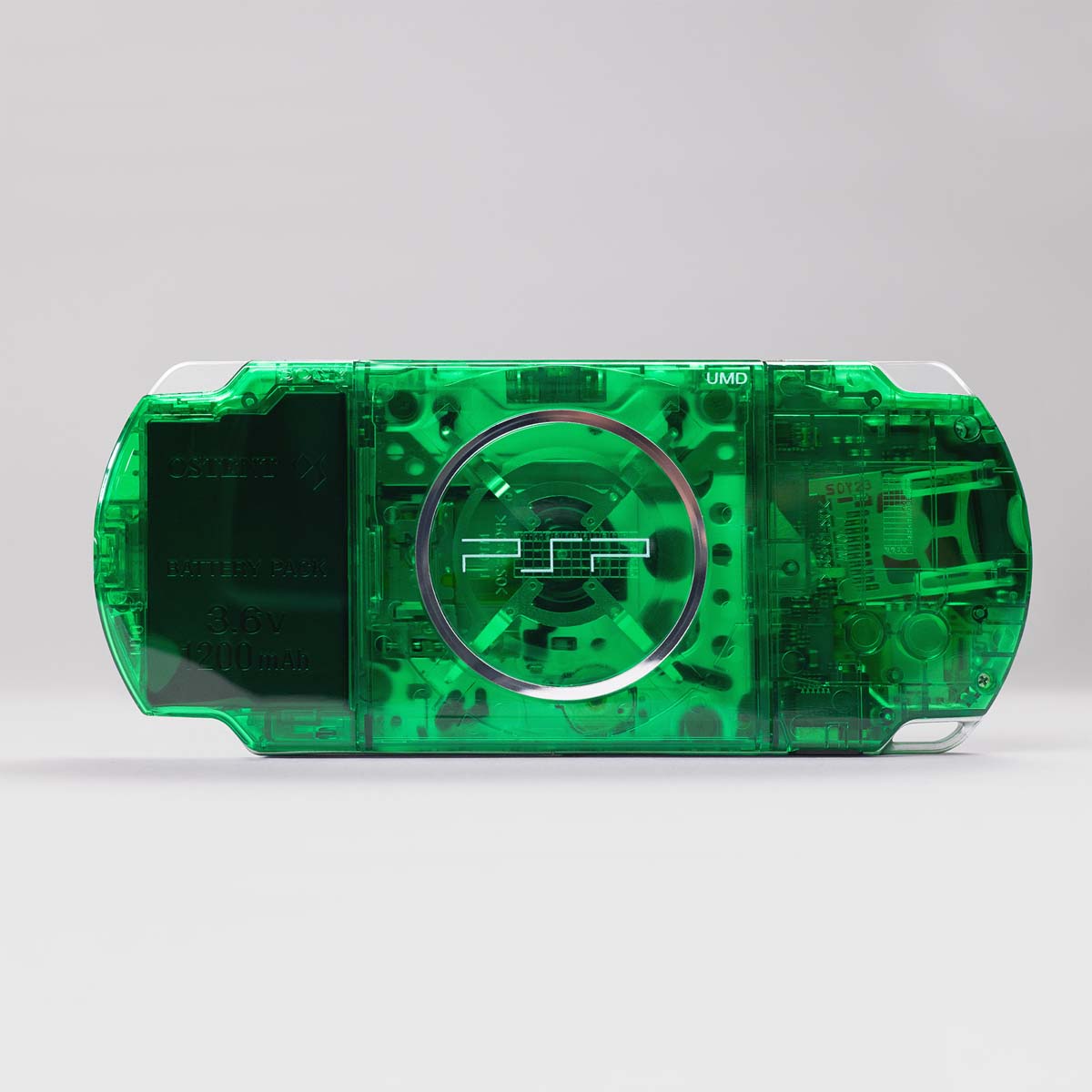 Back view of a green transparent PSP console featuring a visible UMD drive and an OSTENT 3.6V 1200mAh battery inside a clear shell housing