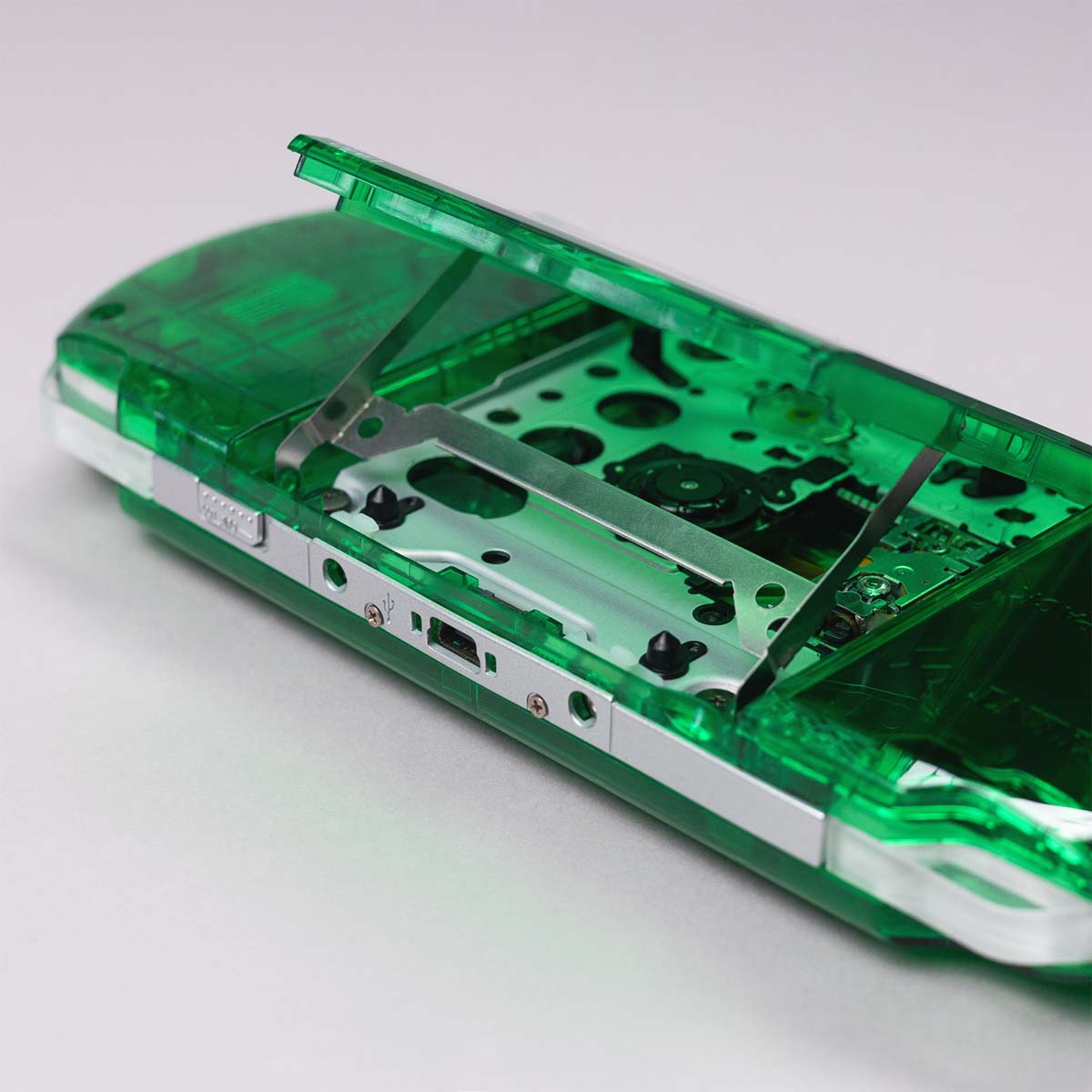Close-up of a green transparent PSP with UMD drive door open, revealing internal disc tray and laser mechanism under custom clear shell