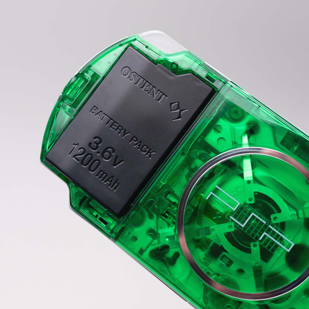 Close-up of a green transparent Sony PSP showing OSTENT 3.6V 1200mAh battery pack and UMD drive through a clear custom shell