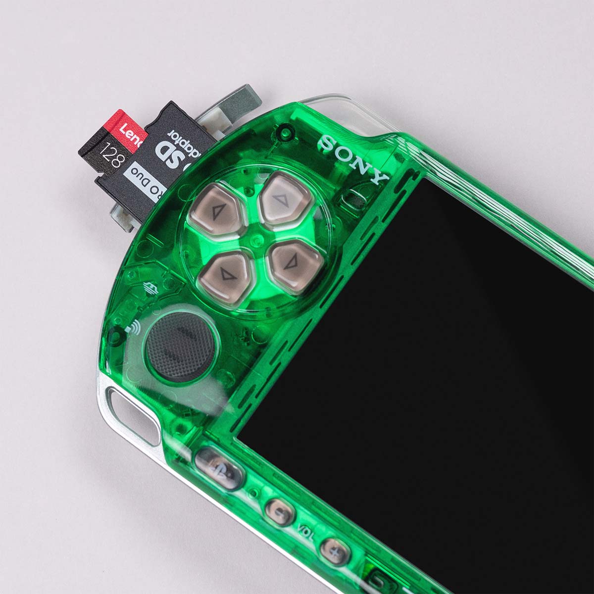 Close-up of a green transparent PSP with white buttons and a 128GB Lexar microSD card inserted via a Memory Stick Pro Duo adapter