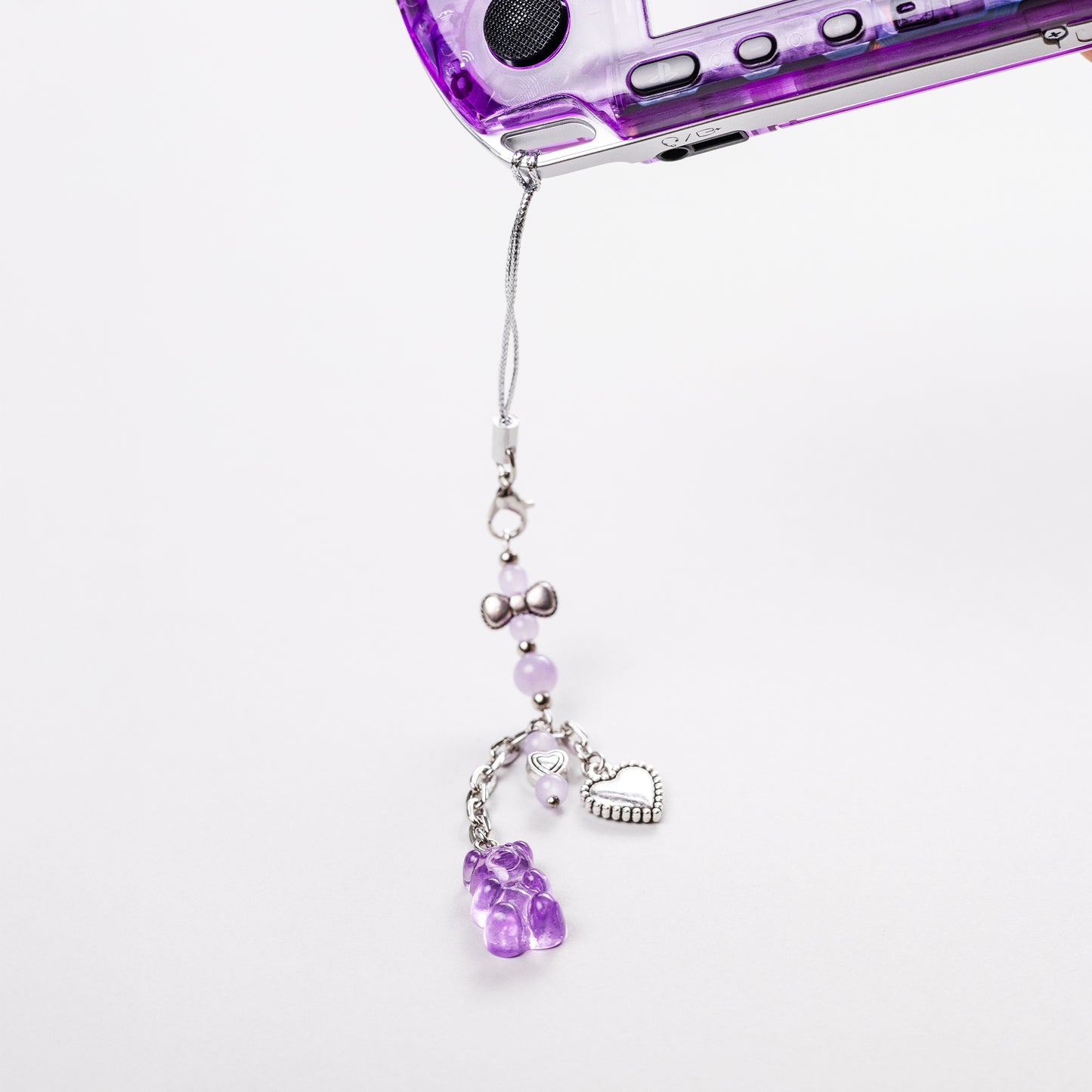 Purple transparent PSP console with attached kawaii charm featuring lilac beads, silver heart, and a purple gummy bear pendant