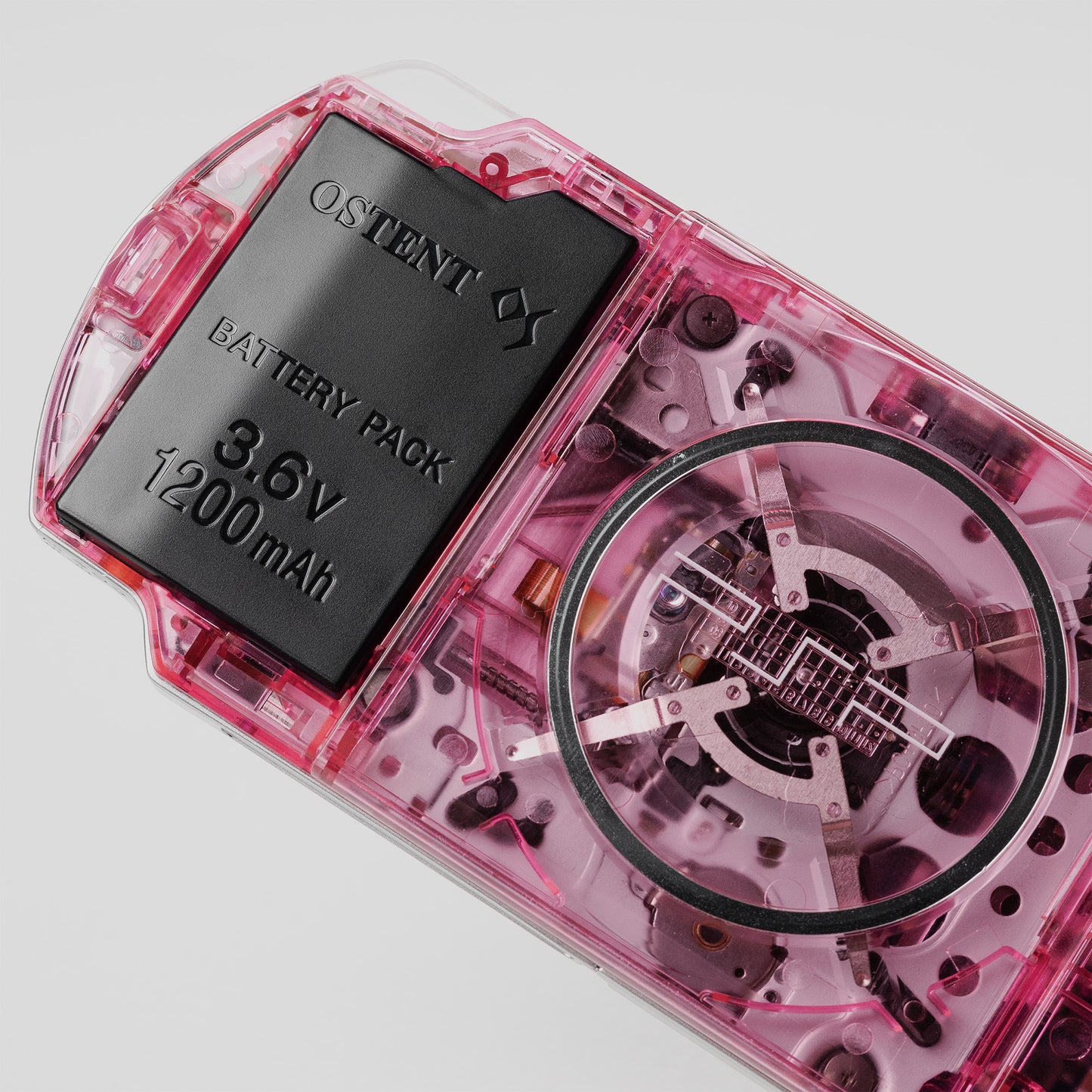 Close-up of a custom pink PSP showing transparent back shell, UMD drive internals, and OSTENT 3.6V 1200mAh battery pack