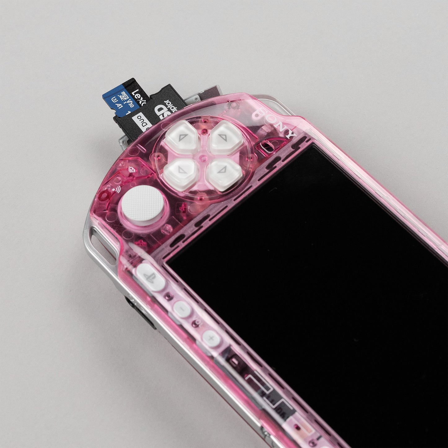 Close-up of a modded pink PSP with transparent shell, white buttons, and a dual-slot microSD to Memory Stick Duo adapter inserted
