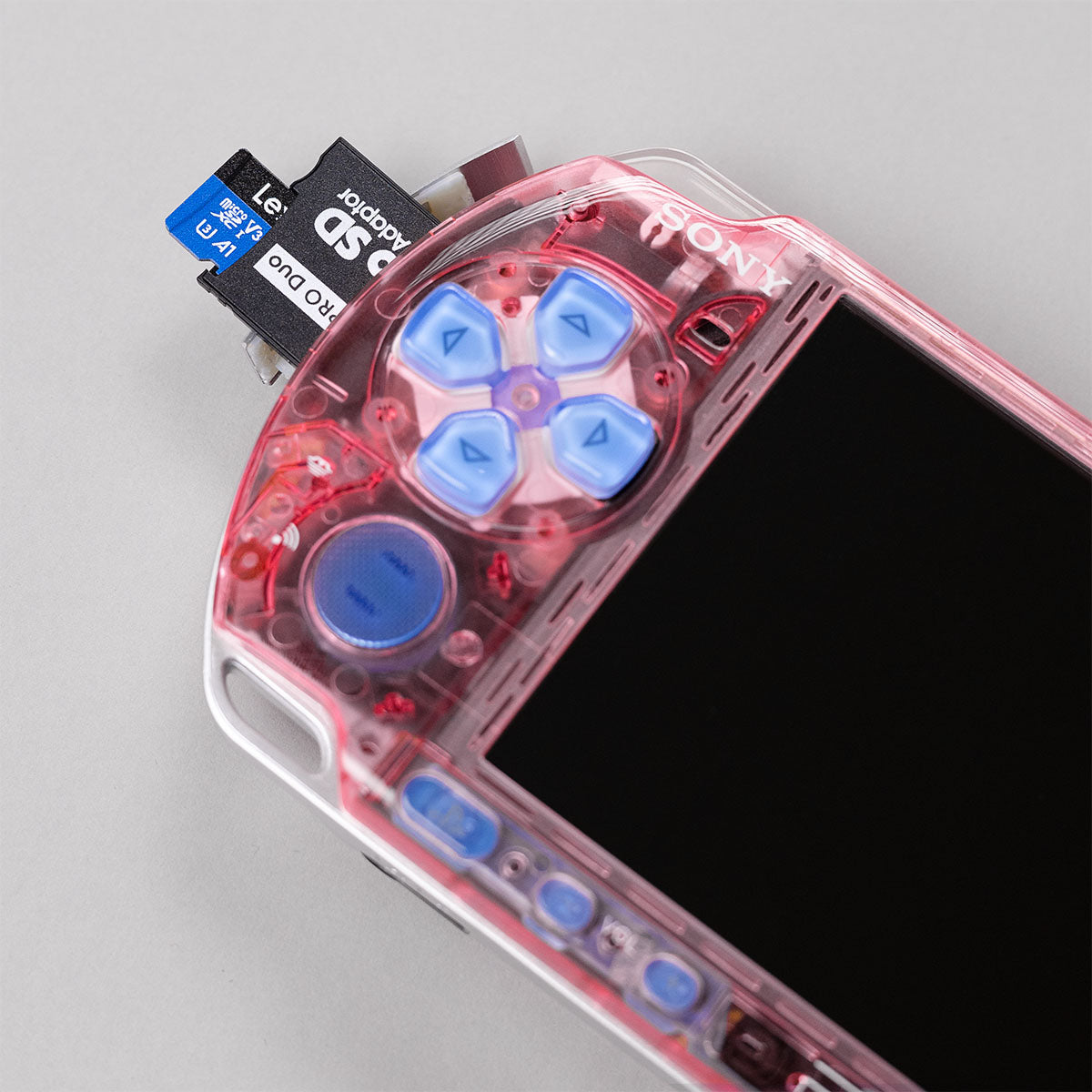 Close-up of pink transparent PSP 3000 with blue buttons, showing Pro Duo SD card adapter upgrade for expanded storage