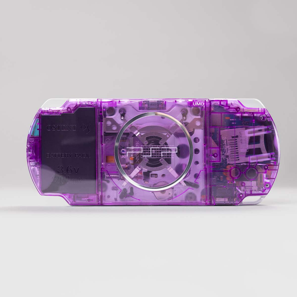 Rear view of a purple transparent PSP console with visible UMD drive and OSTENT 3.6V 1200mAh battery pack, part of a black button custom build