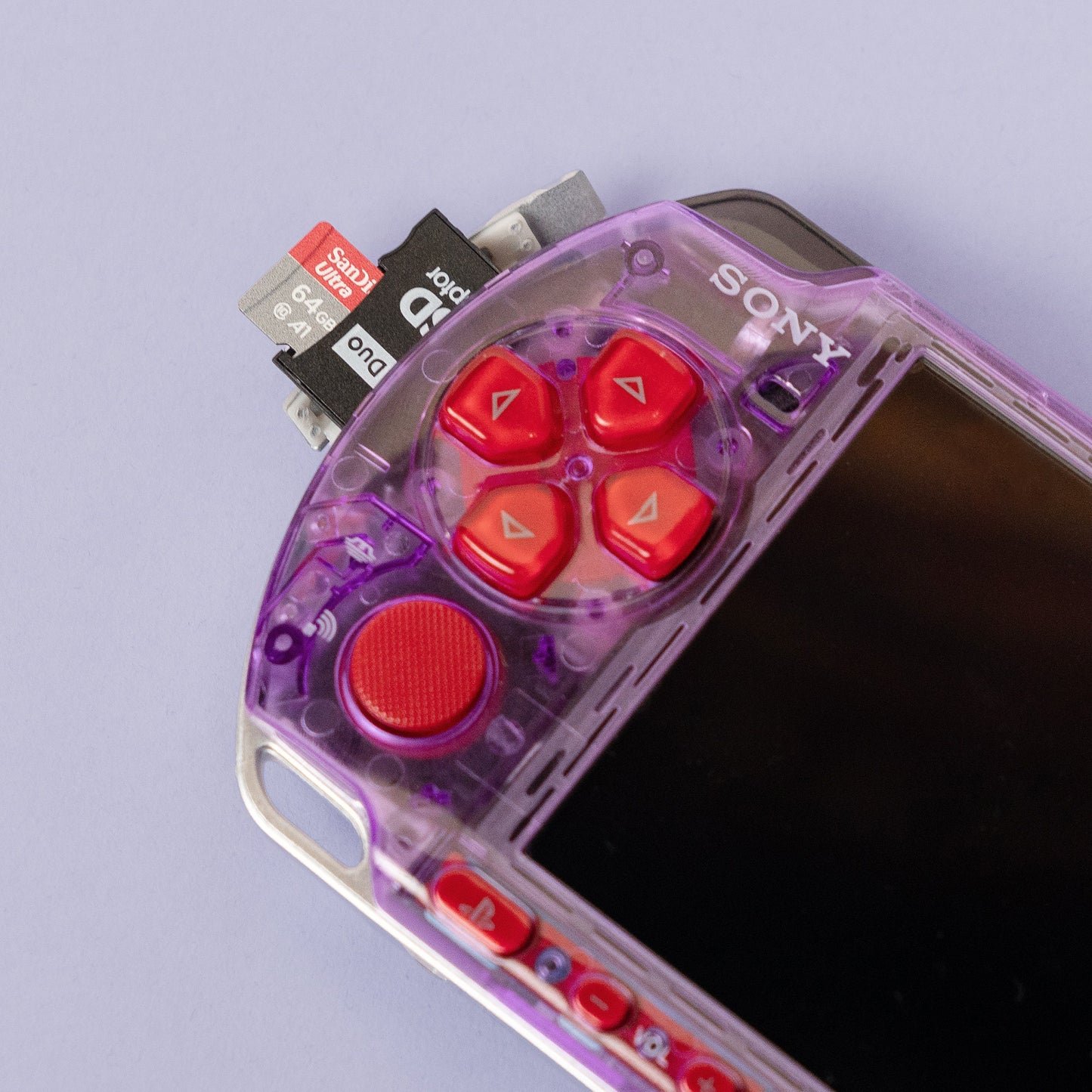 Close-up of a purple transparent PSP with red buttons and a 128GB SanDisk microSD inserted into a Memory Stick Pro Duo adapter for expanded storage