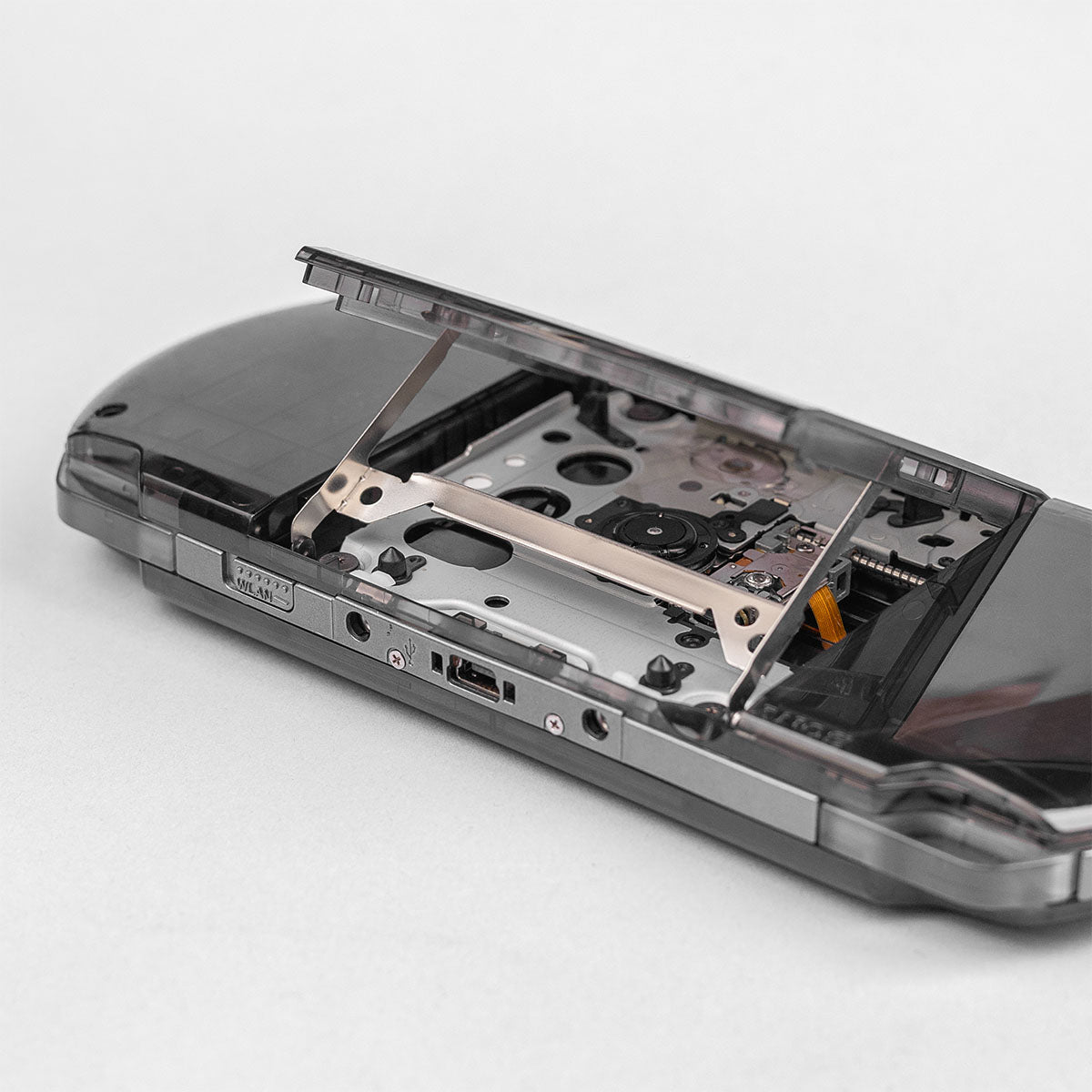 Detailed view of a smoke black transparent PSP with the UMD drive door open, exposing the laser mechanism and disc tray in clean condition