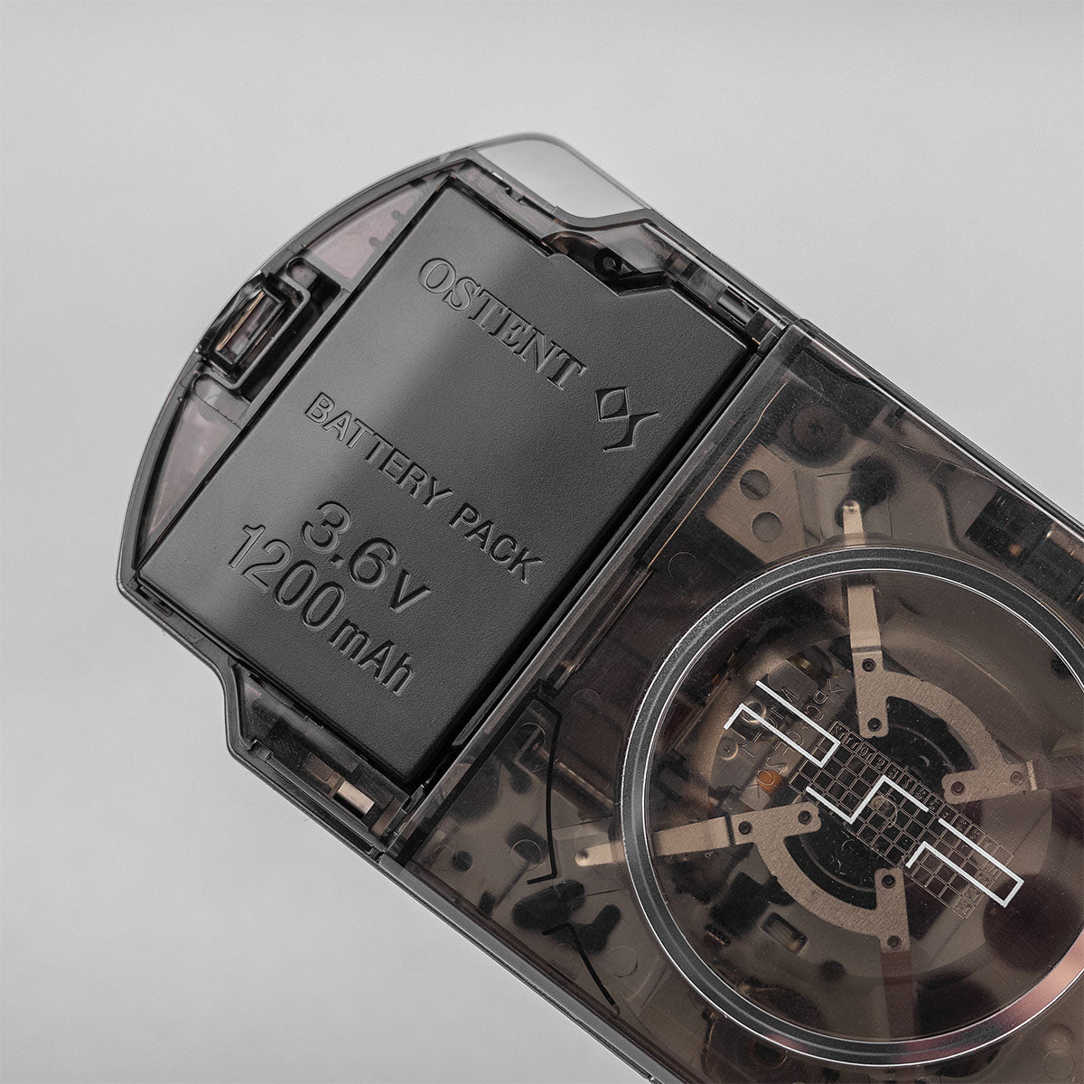 Close-up of a smoke black transparent PSP featuring an OSTENT 3.6V 1200mAh battery pack and visible UMD drive under the clear rear shell