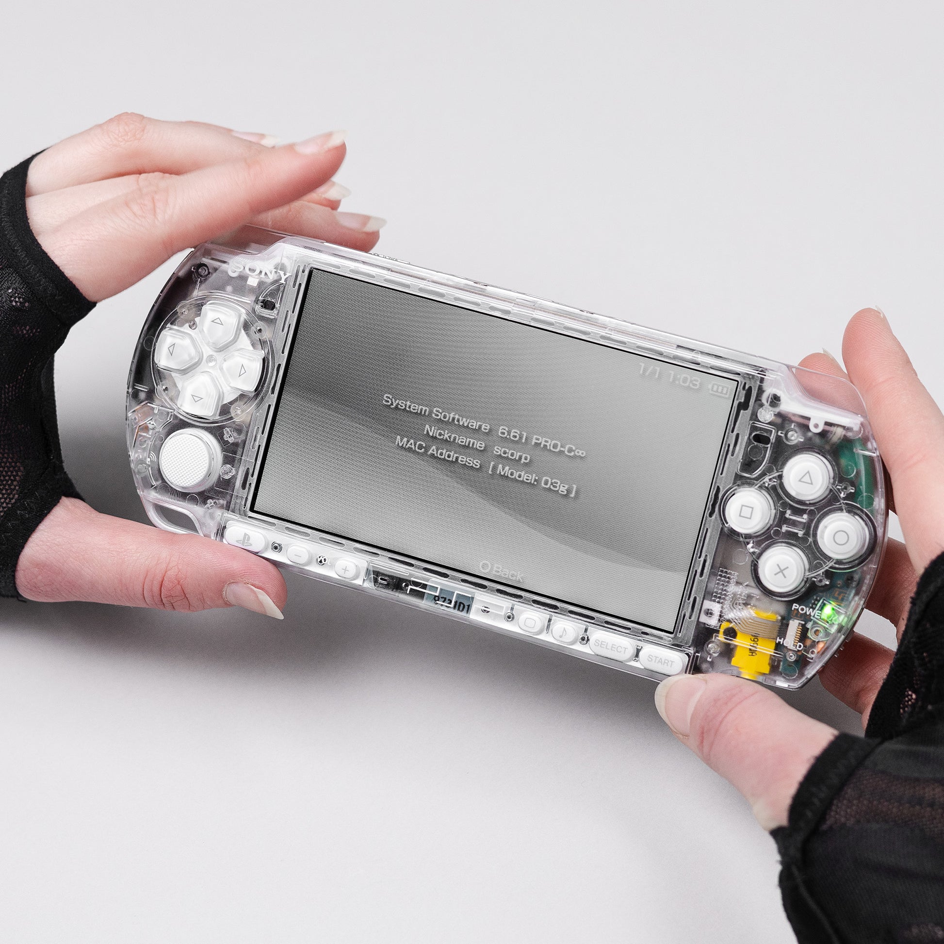 Sony PSP handheld console with transparent shell and white buttons running firmware 6.61 PRO-C, held in hands wearing fingerless gloves