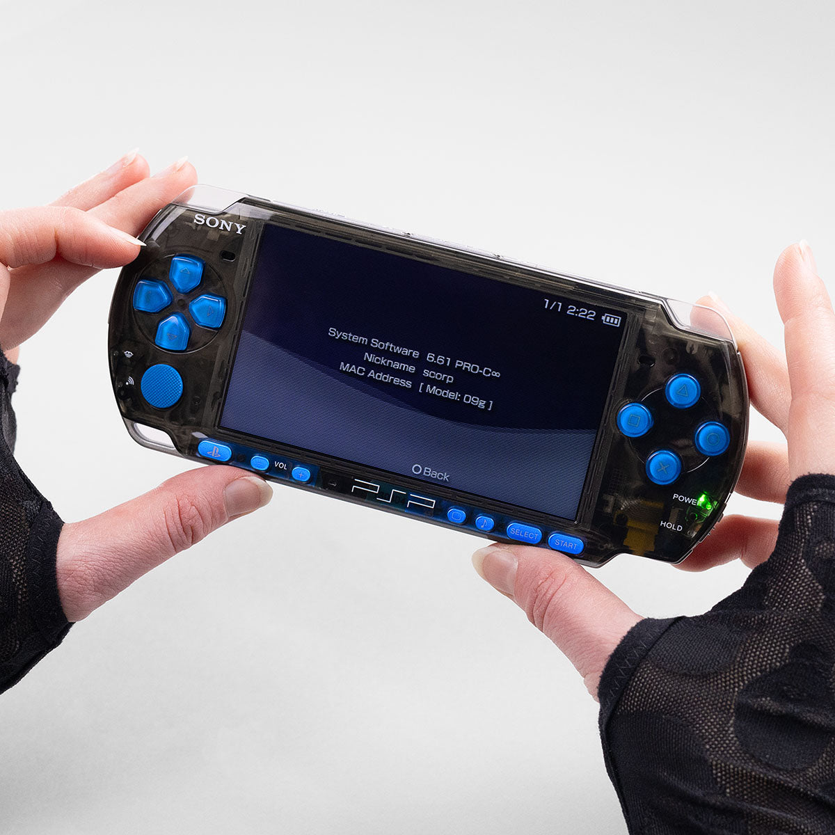 A transparent black PSP-3000 handheld console with blue buttons running custom firmware, held in gloved hands against a clean white background.