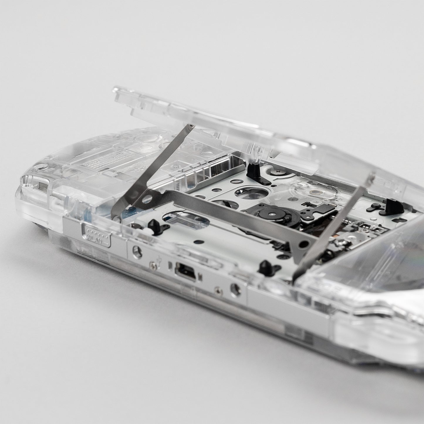 Close-up of an open UMD drive on a Sony PSP with a custom transparent clear shell, showing internal disc tray and mechanical components