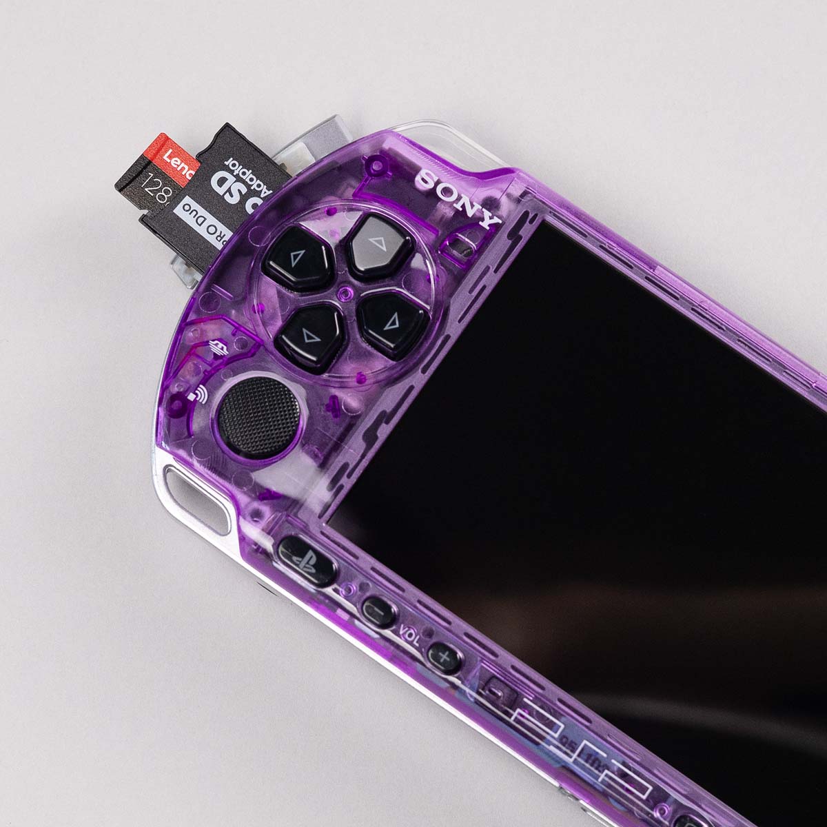 Close-up of a purple transparent PSP with black buttons and a 128GB microSD card inserted via a Memory Stick Pro Duo adapter
