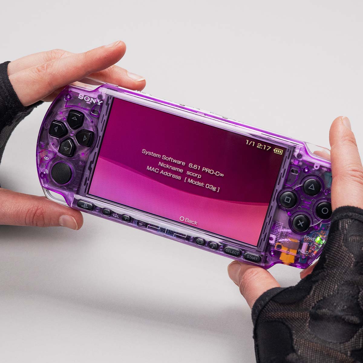 Purple transparent PSP with black buttons running firmware 6.61 PRO-C, held in gloved hands with pink system info screen displayed