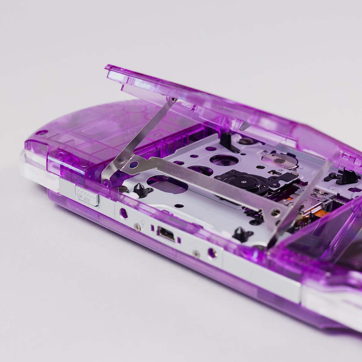 Close-up of a purple transparent PSP with UMD door open, showing internal laser assembly and disc tray under clear shell construction