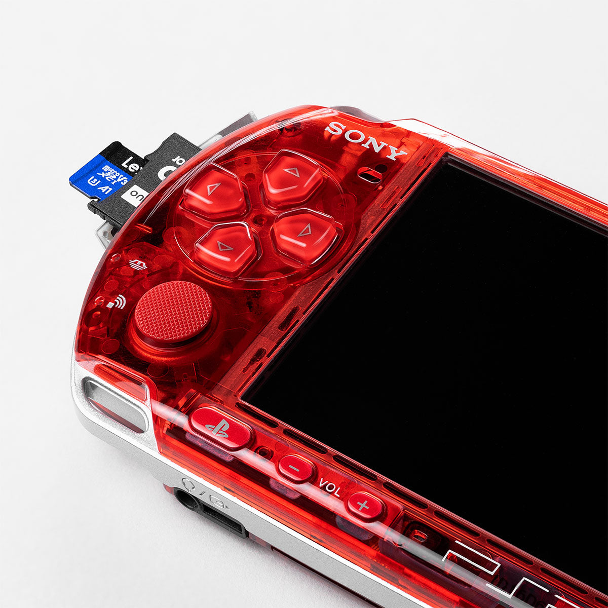 Close-up of Sony PSP 3000 in transparent red custom shell showing buttons, analog stick, and inserted memory card.